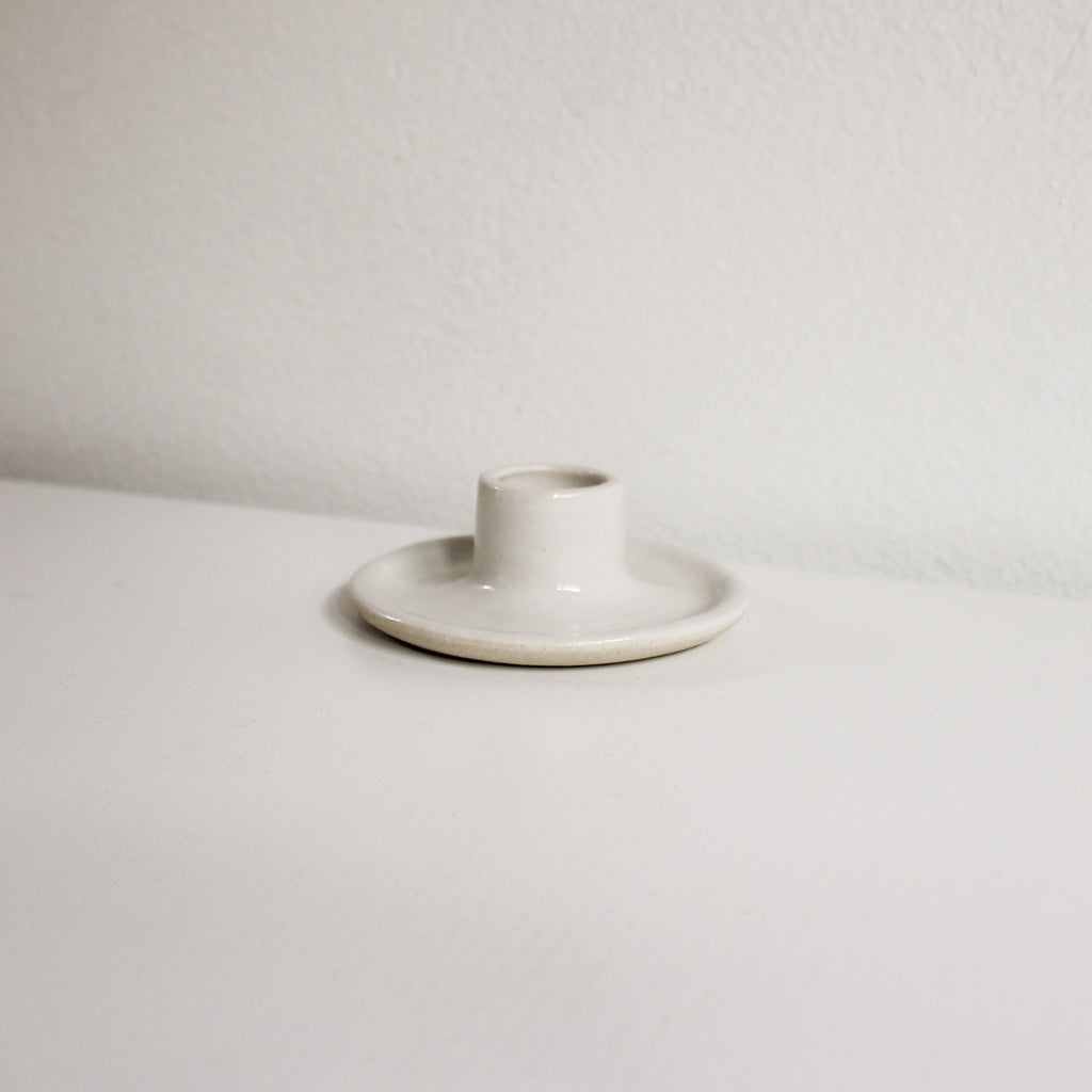 A taper candle holder made of white clay with white glaze sitting on a white table.