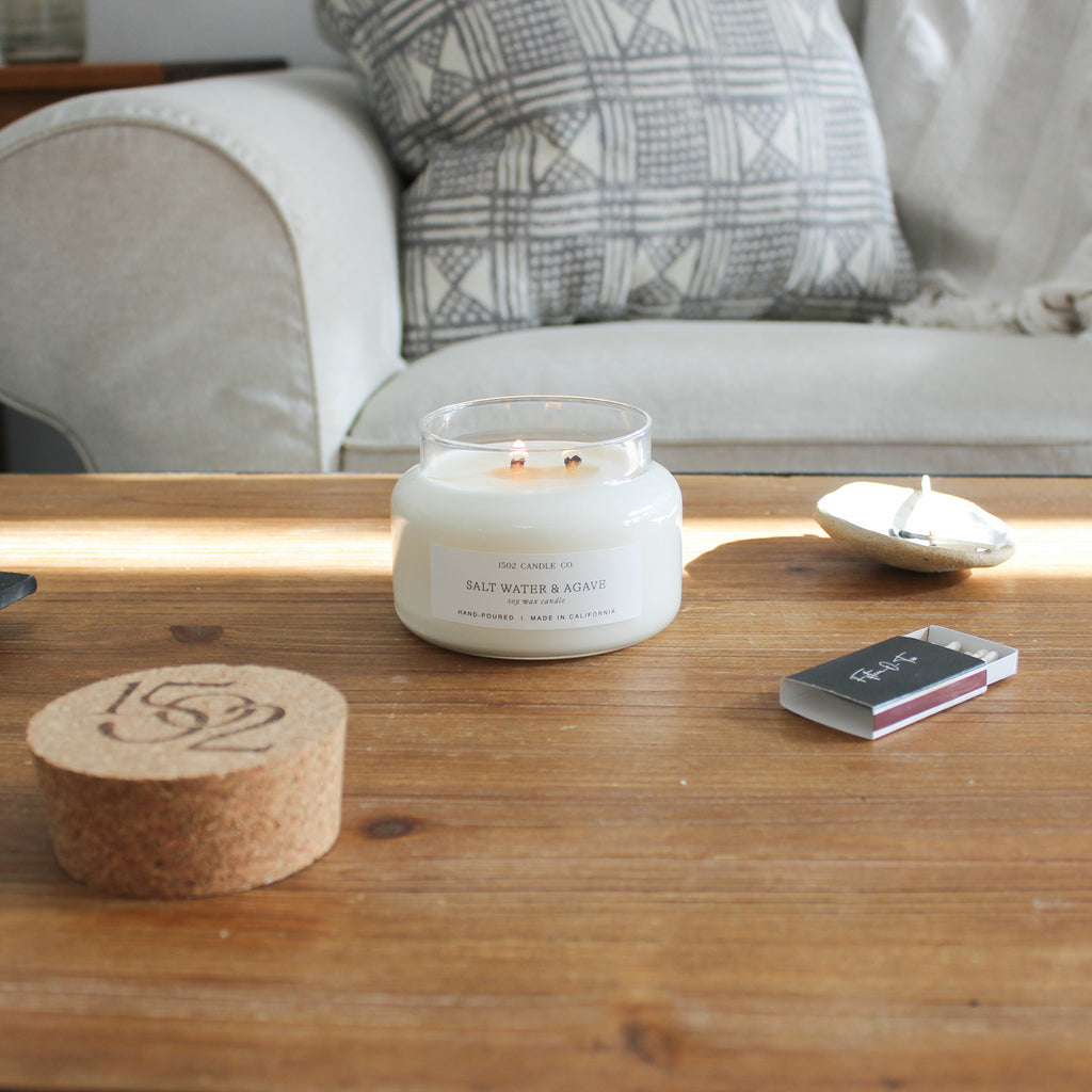 Salt water and agave soy wax candle lit on a wooden table in a california modern living room.