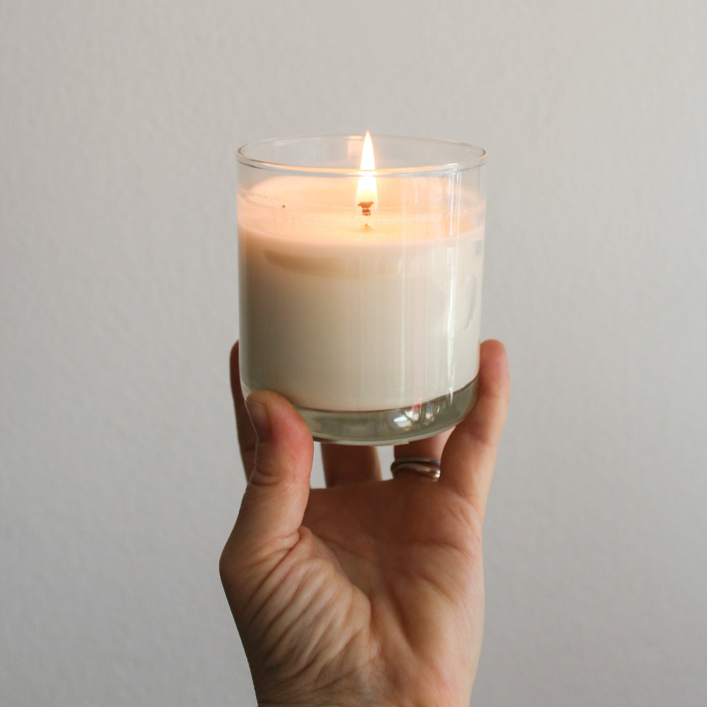 a light skinned hand holding up a lit Monstera Leaf and Aloe soy wax reusable candle.