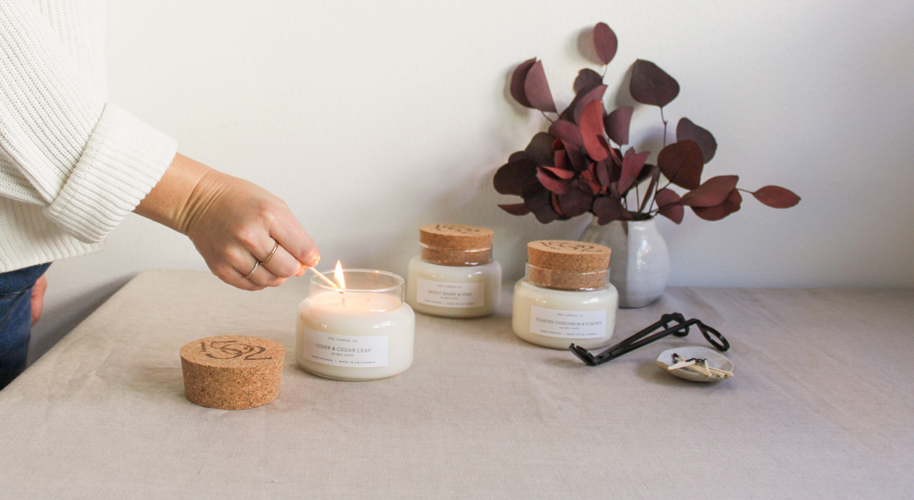 A ligh skined hand lights a Cider and Cedar leaf candle.