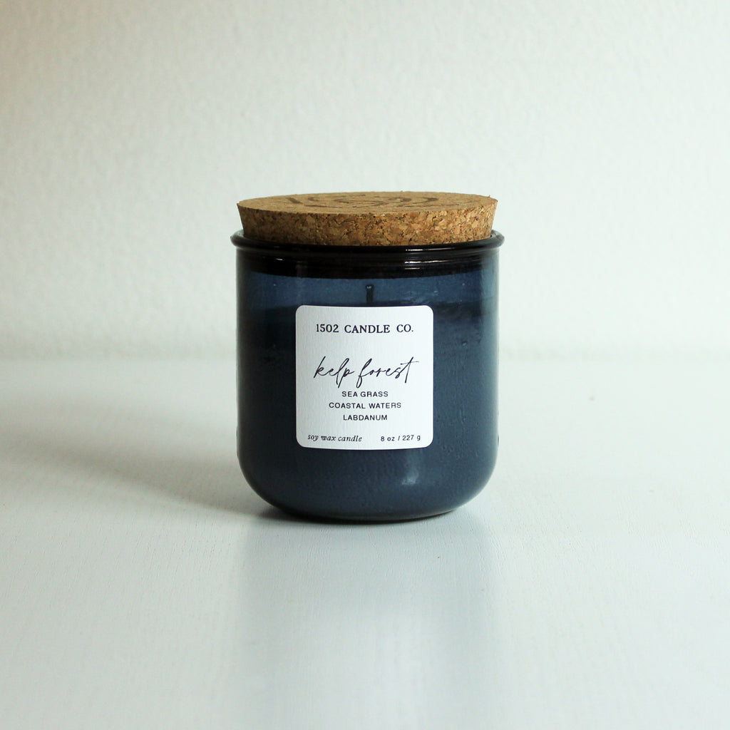 Candle in a moody ocean blue jar with a natural cork lid on a light background