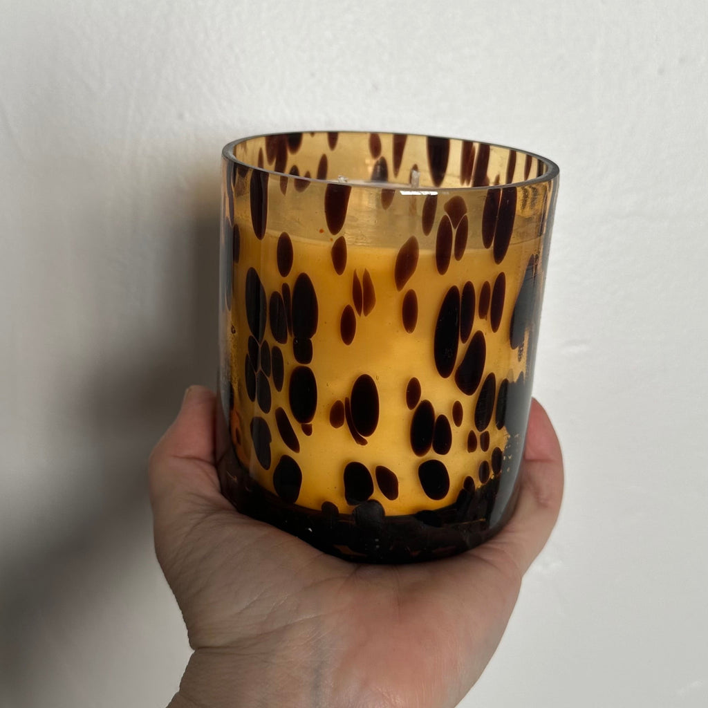 Hand holding a leopard print candle holder against a plain background