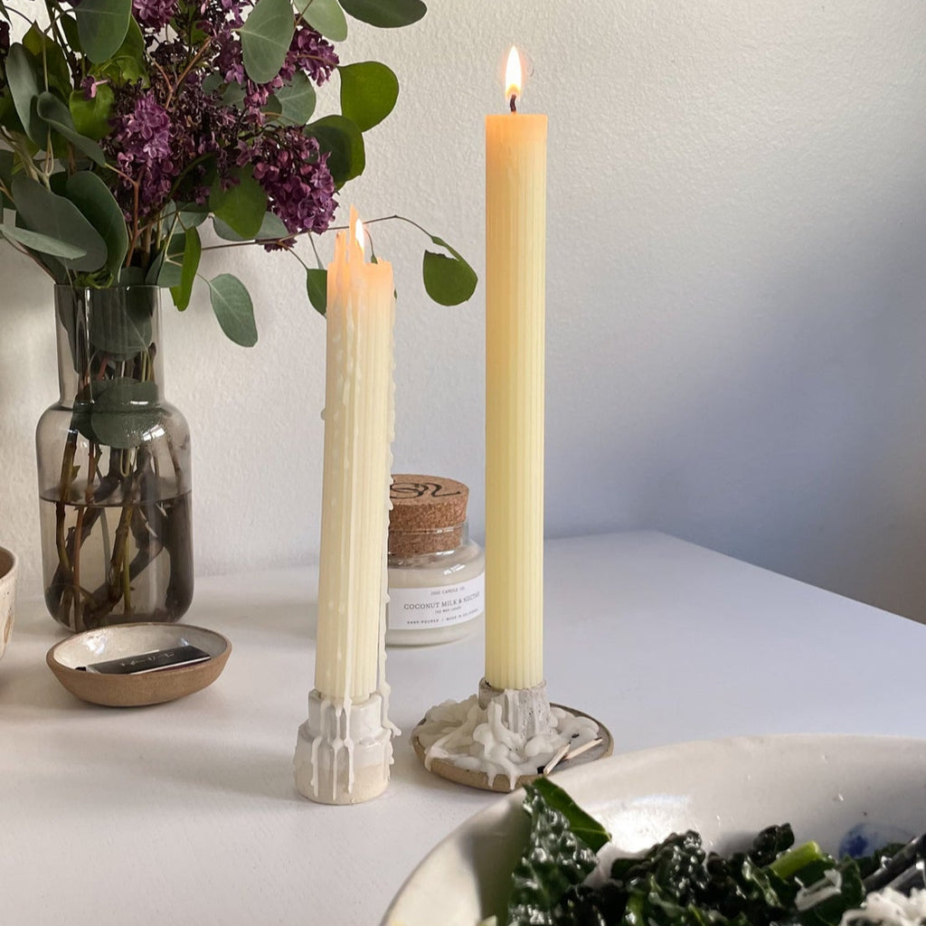A pair of lit beeswax taper candles on a white table at dinnertime. 