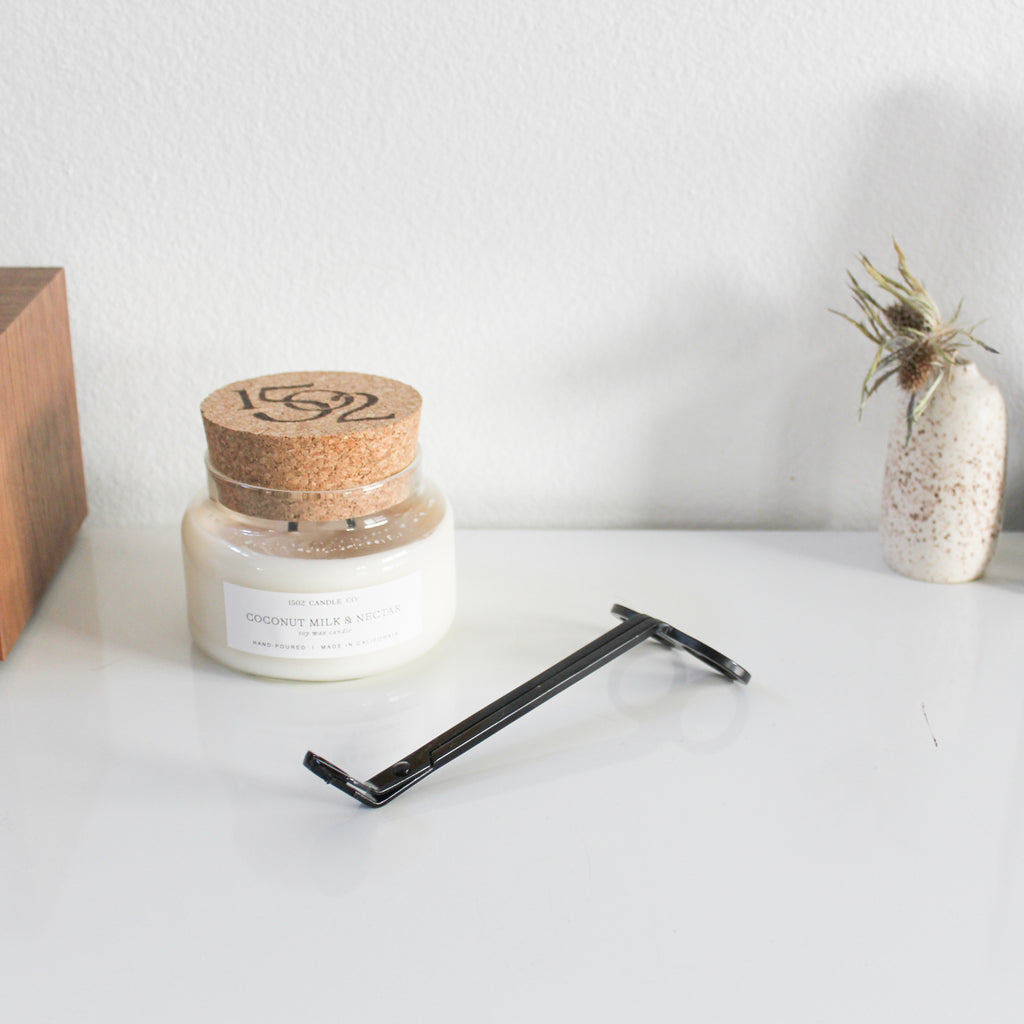 A black wick trimmer sits next to a 1502 Candle Co. soy wax candle.
