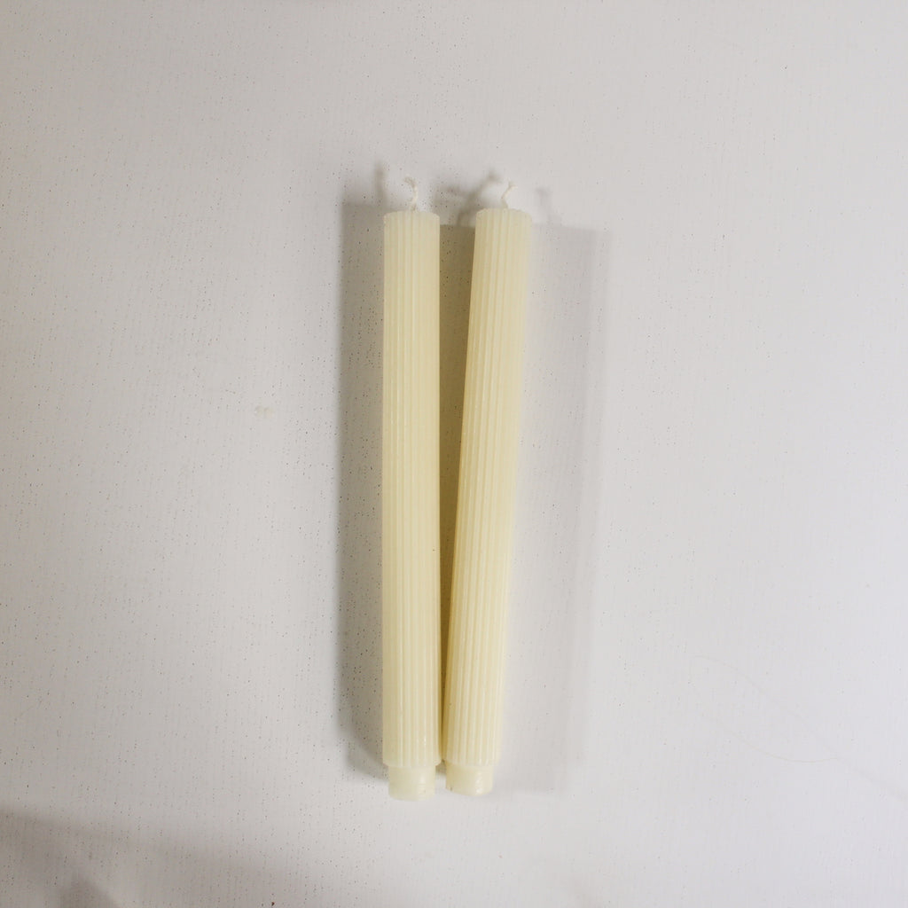 A pair of beeswax taper candles laying against a white surface.