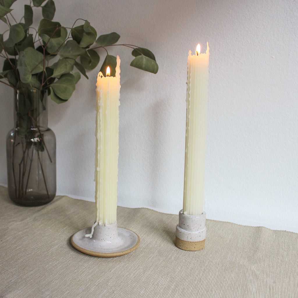 A pair of taper candle holders made of brownish speckled clay with white glaze holding lit beeswax taper candles at dinnertime. 