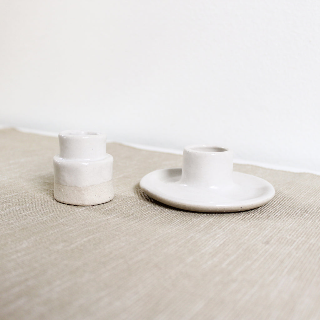 A pair of taper candle holders made of white clay with white glaze on a linen covered table.