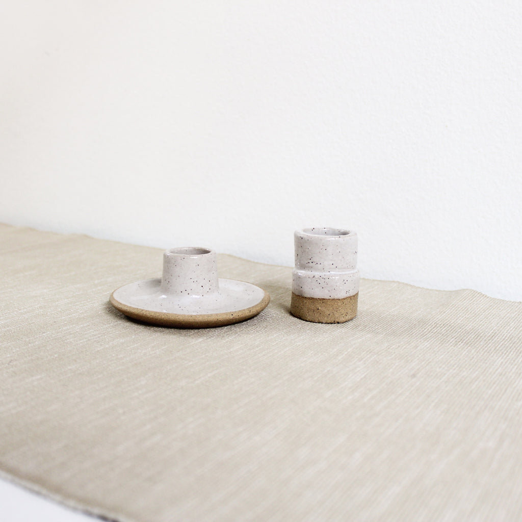 A pair of taper candle holders made of brownish speckled clay with white glaze on a linen covered table.