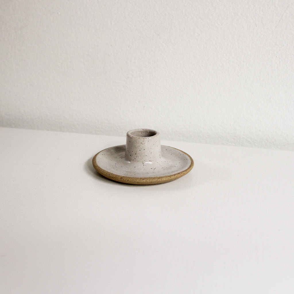 A taper candle holder made of brownish speckled clay with white glaze sitting on a white table.