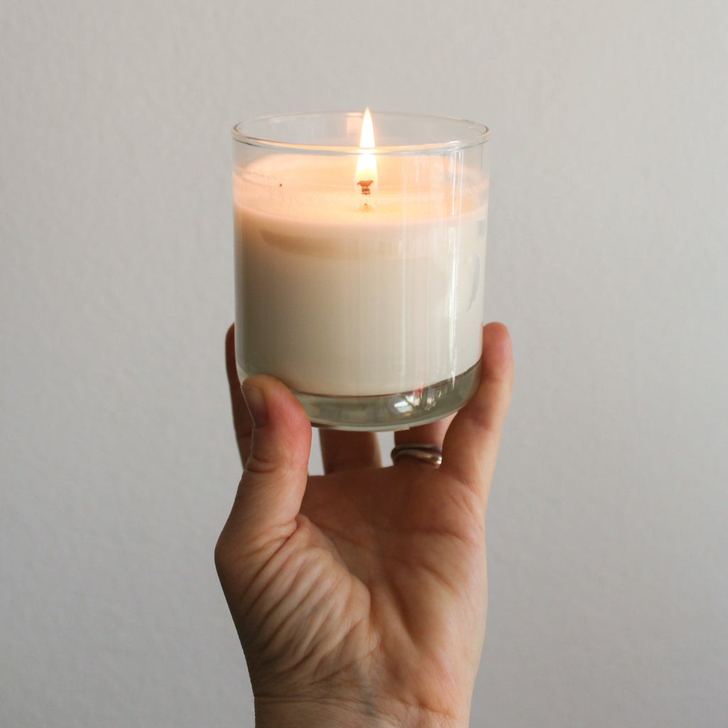a light skinned hand holding a lit Salt Water and Agave soy wax reusable candle.