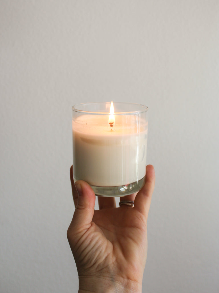 a light skinned hand holding up a lit Monstera Leaf and Aloe soy wax reusable candle.