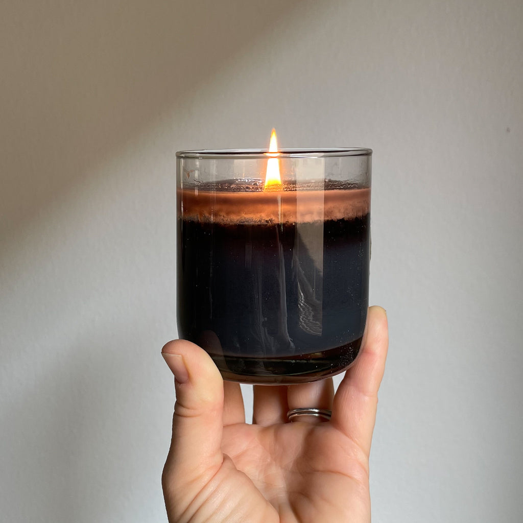 A light skinned hand holds up a lit Black Samhain Halloween soy wax candle.