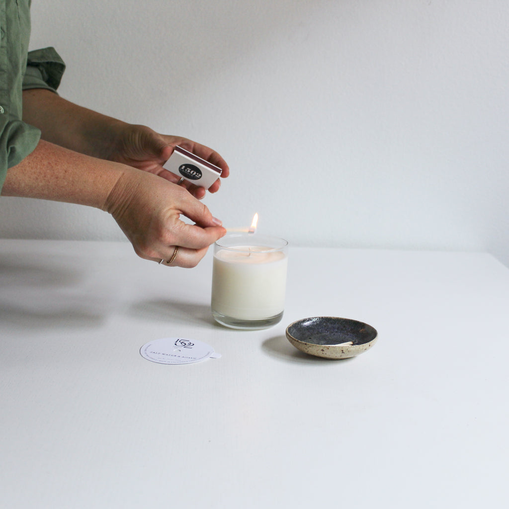 a Juniper and Hinoki soy wax reusable candle being lit by a light skinned person 
